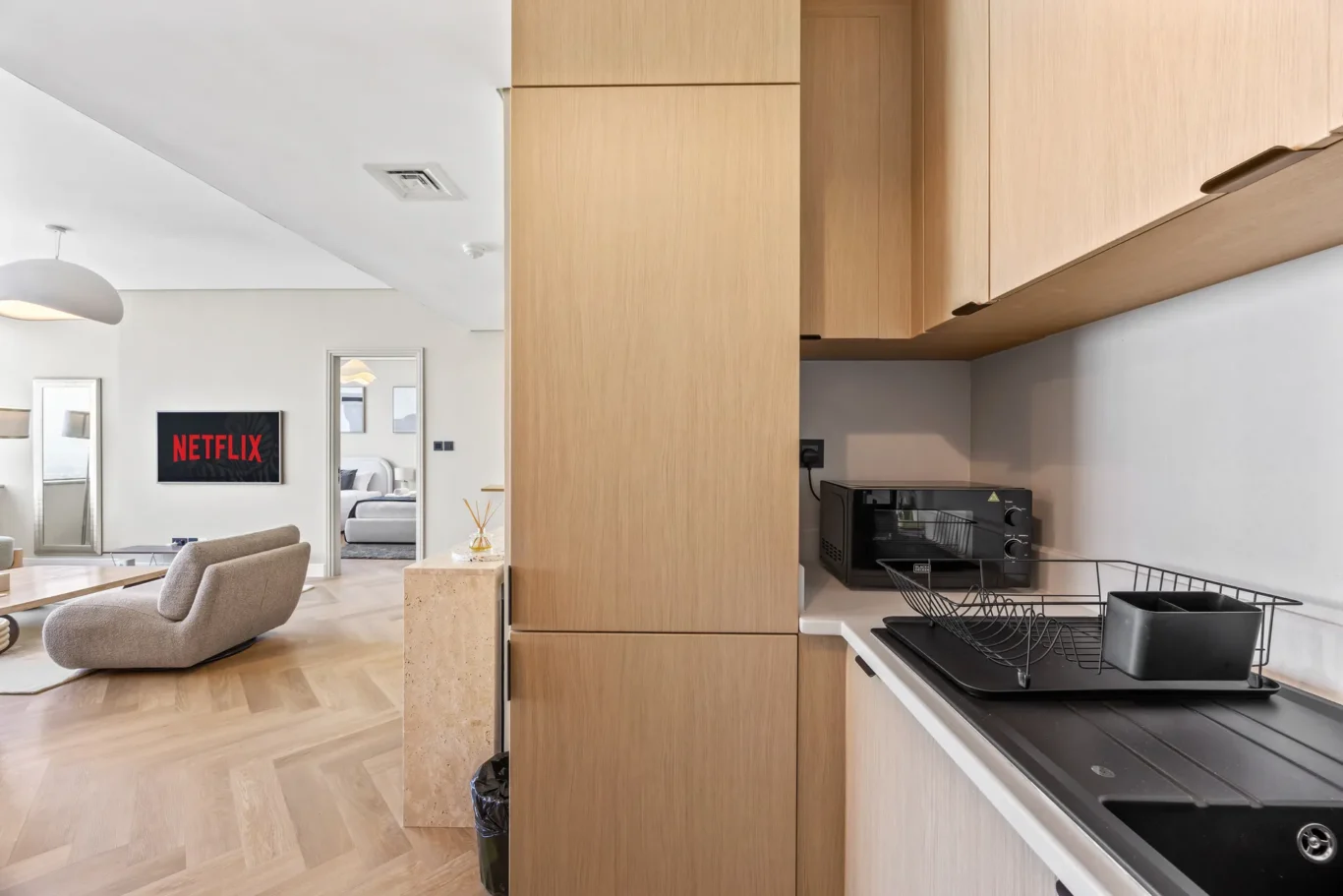 Open-plan living area and kitchen in a modern apartment; wall-mounted TV displays Netflix in the living space.