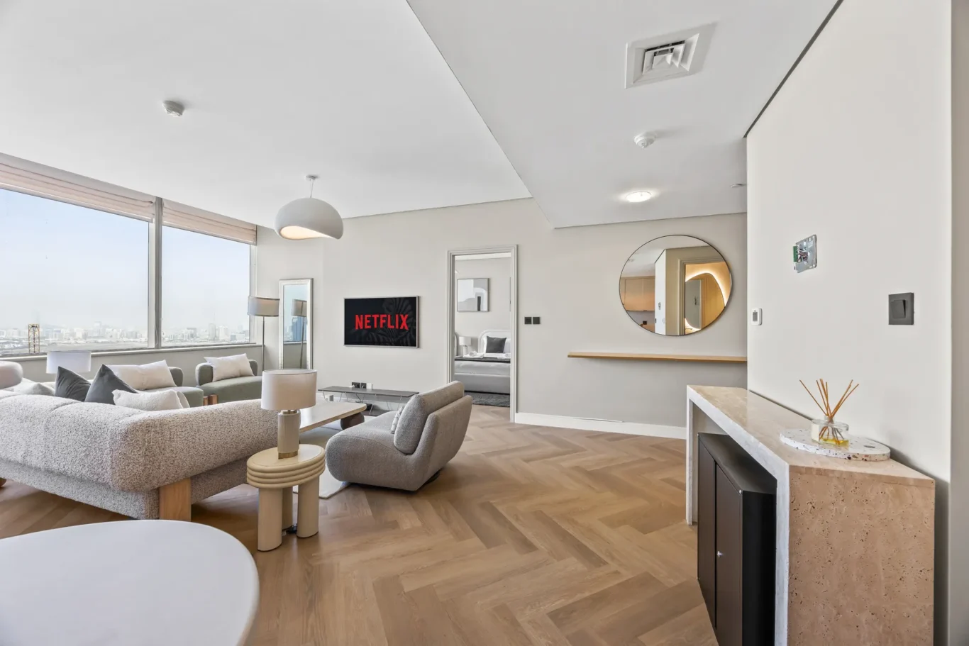 Modern open-plan living room with a large window view and a wall-mounted Netflix screen above a gray sofa.