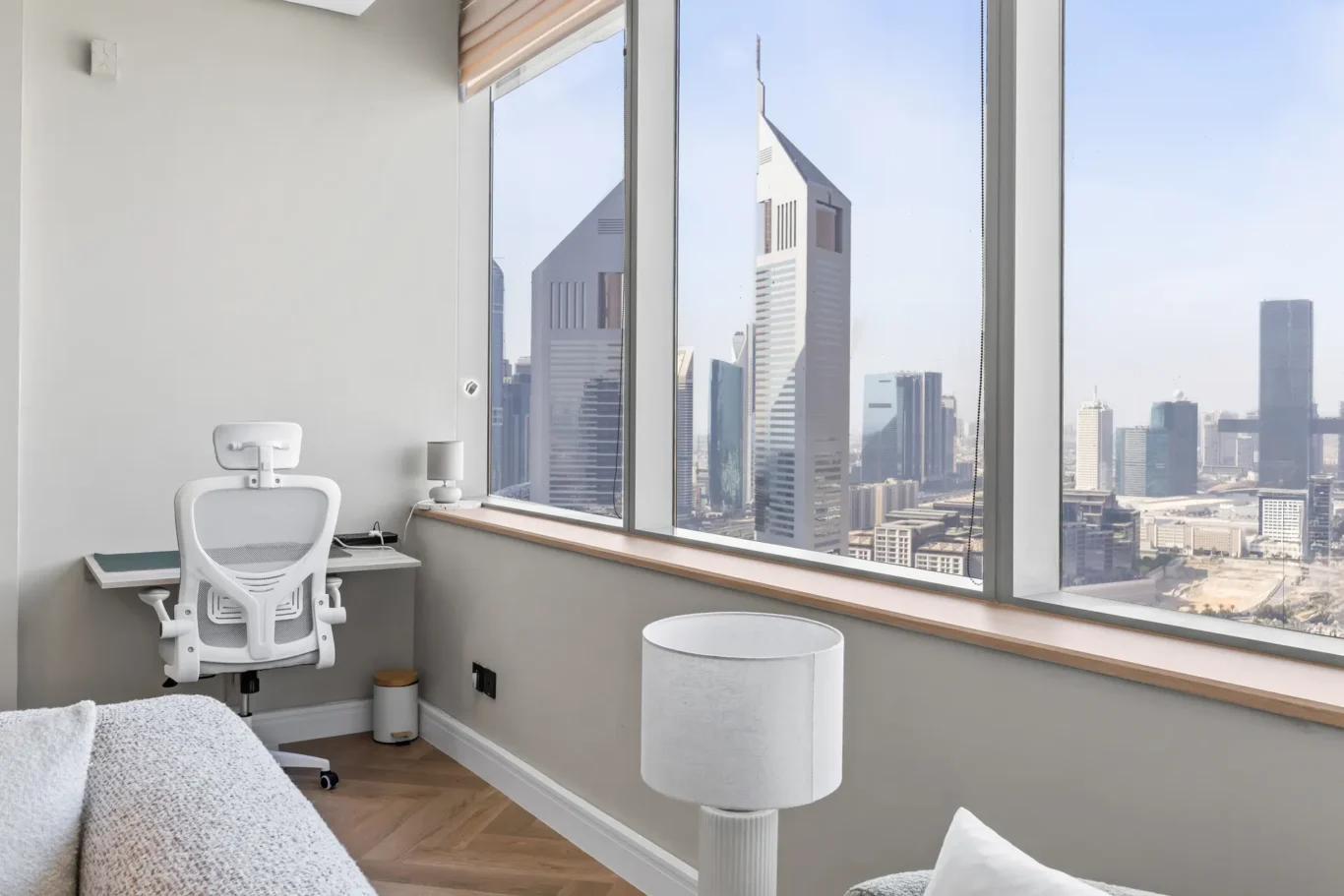 Bright home office with a city skyline view; white ergonomic chair at a desk by large windows.