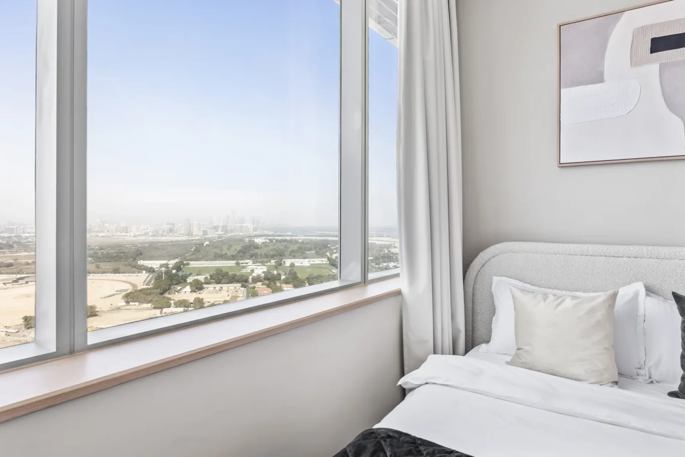 Bedroom with large corner windows overlooking a cityscape, white bedding, and abstract wall art.