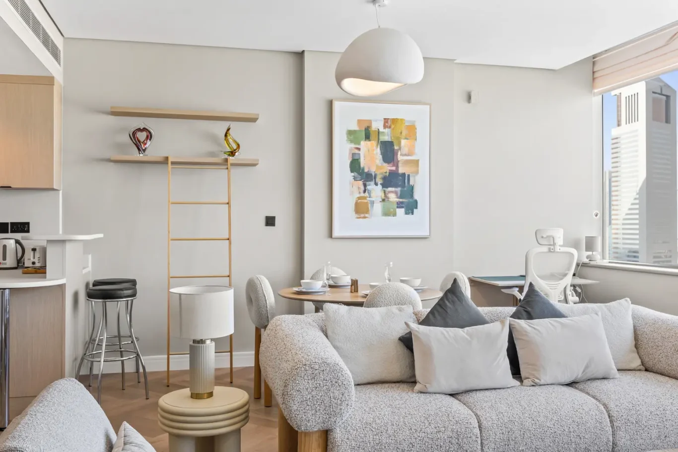 Open-plan living area with a beige sofa, gray cushions, round dining table, and an abstract painting on the wall.