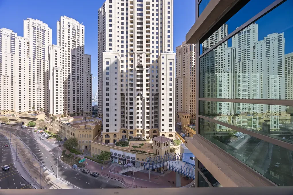 Cluster of tall white residential towers with a glass-fronted building on the right, under a bright blue sky. Conveys an urban cityscape.] ,