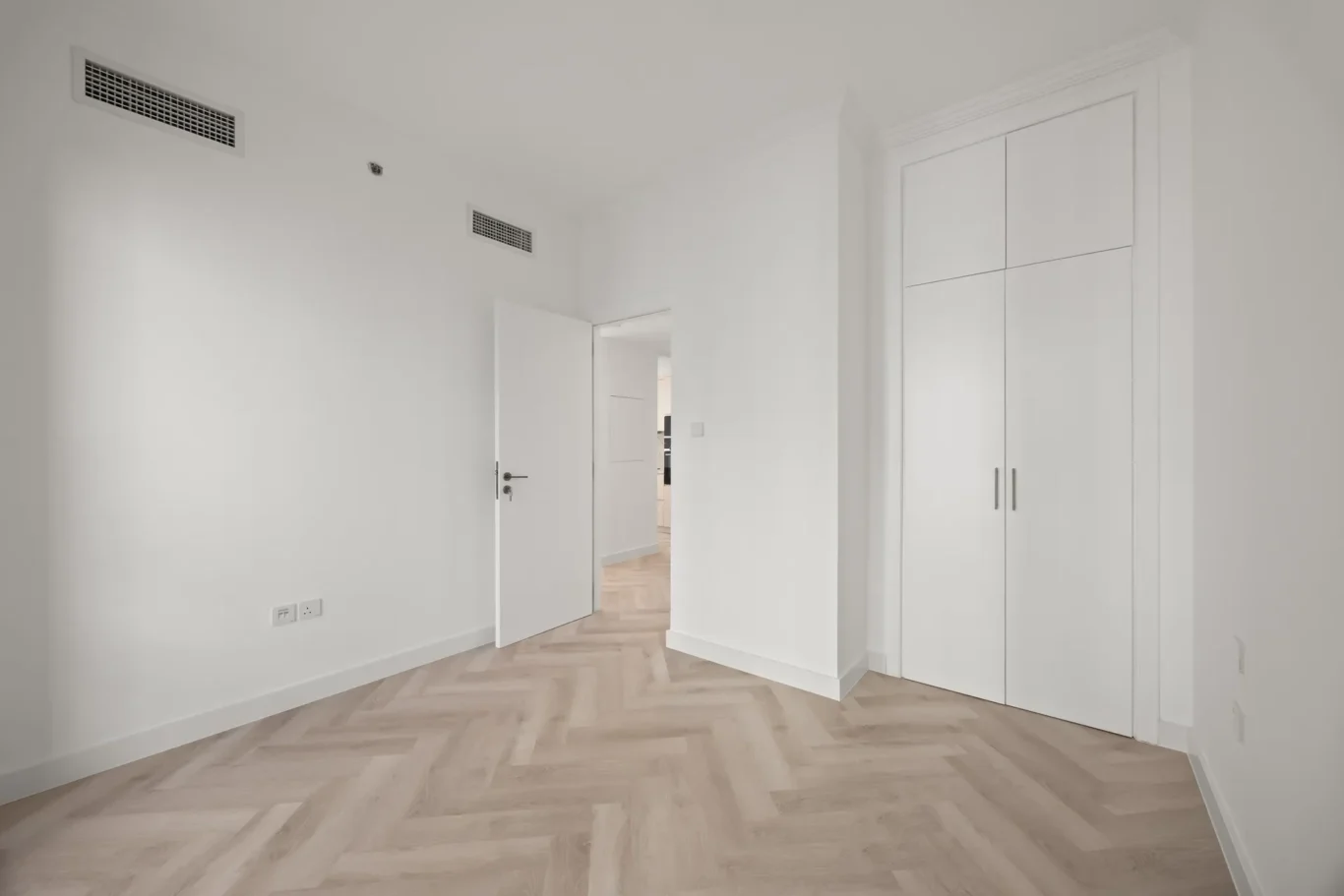 White minimalist hallway with light wood herringbone floor, an open door to another room, and a large white built-in closet on the right.