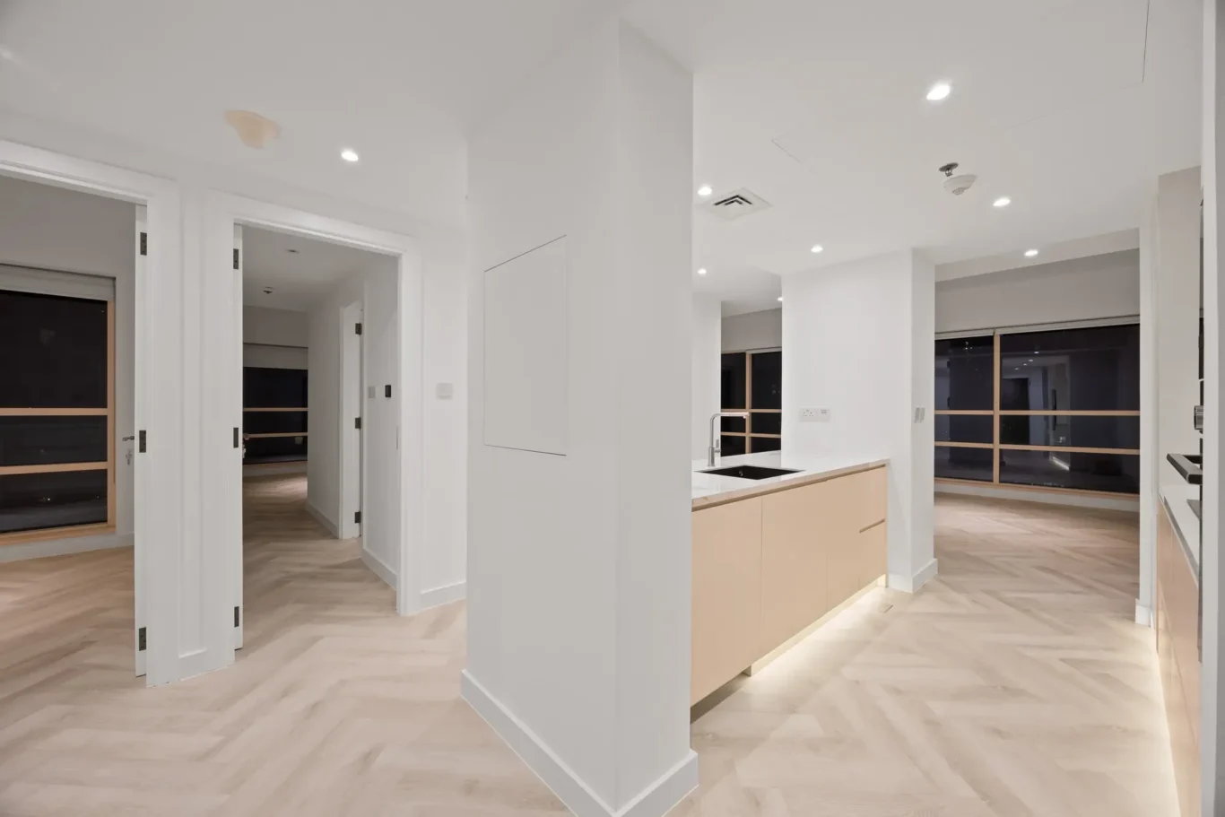 Bright, modern kitchen with a light wood island, white cabinets, and large windows letting in night light.