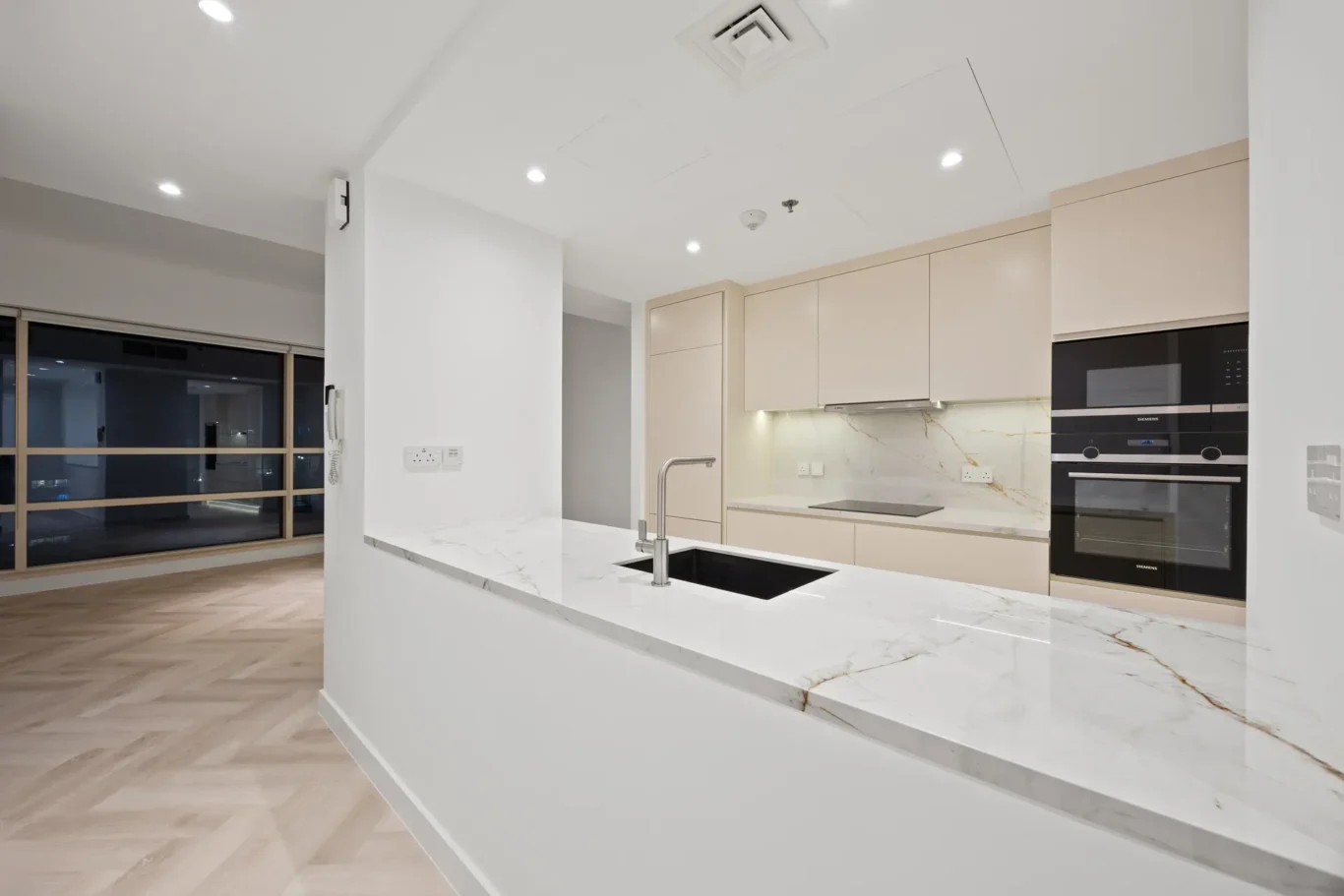 Contemporary kitchen with white cabinets, marble countertops, and an island sink with a chrome faucet; built-in double ovens on the right.