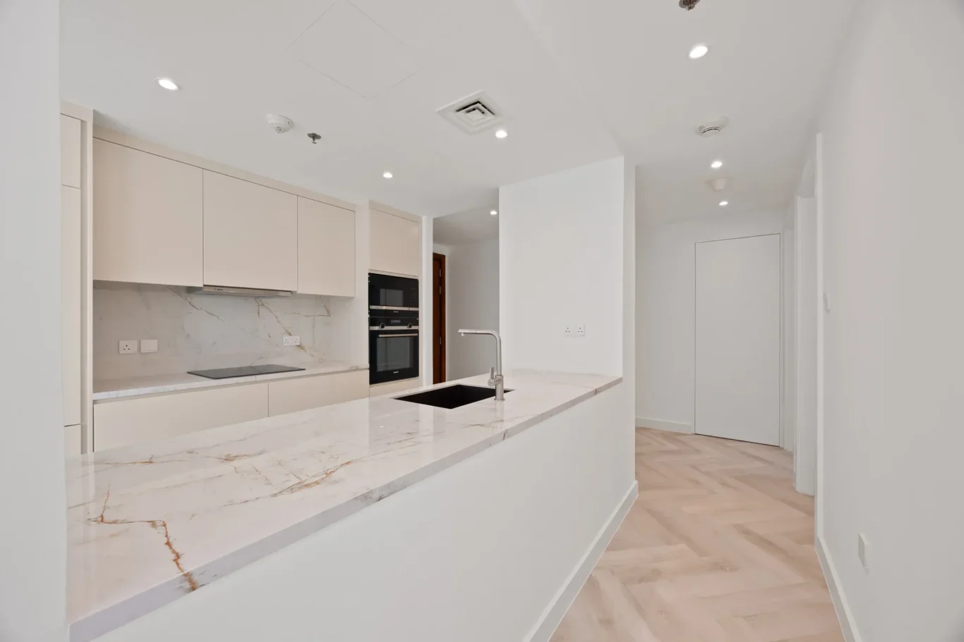 Modern white kitchen with marble island, built-in oven, and light wood floors, bright and open.