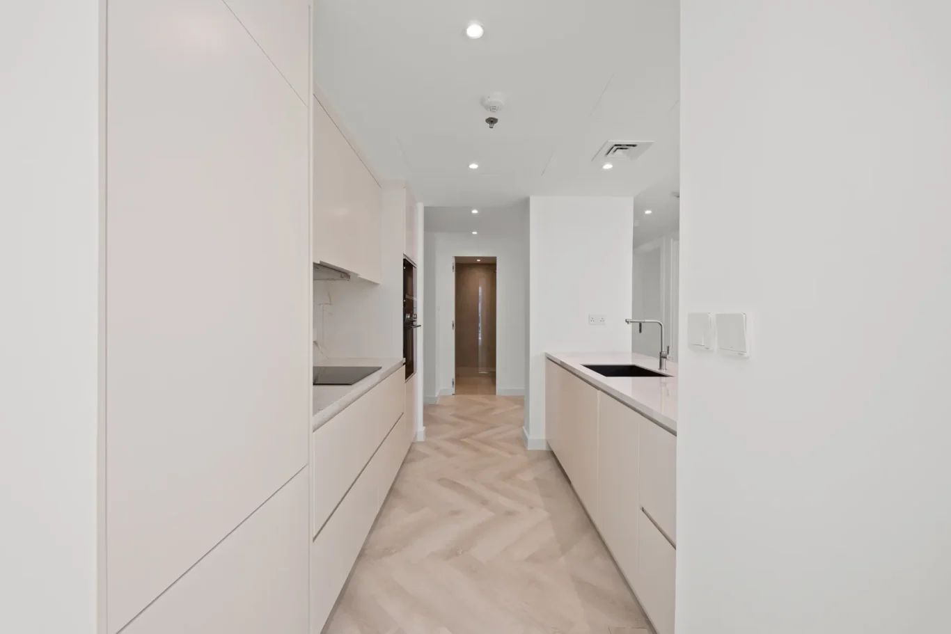 Bright, minimalist kitchen with white cabinets, beige island, and a central sink island; doorway at the far end.
