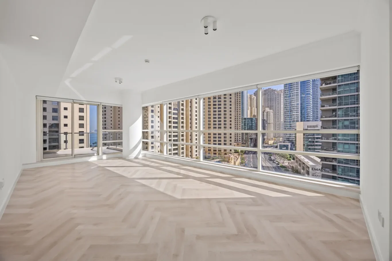 Bright empty living room with large floor-to-ceiling windows overlooking a city skyline outside.