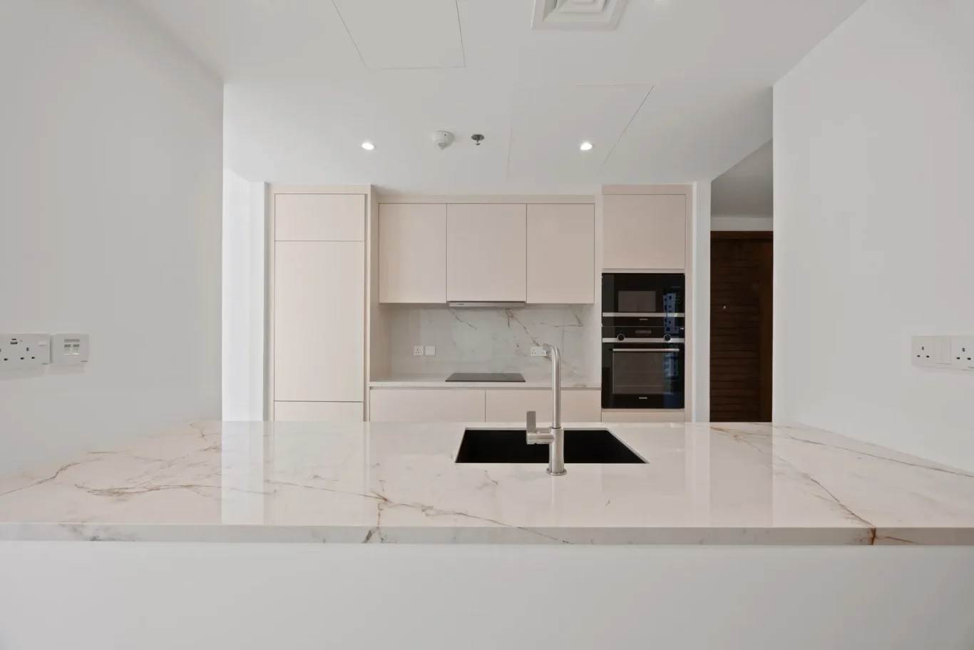 Modern white kitchen with a marble island, built-in oven, and minimalist cabinetry.