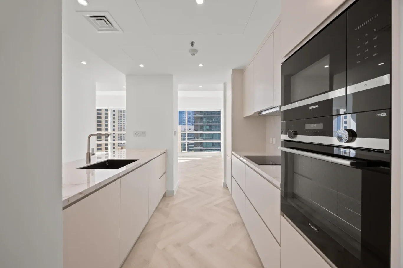 Modern white kitchen with an island, marble countertop, undermount sink, and a wall of built-in Siemens oven units on the right.