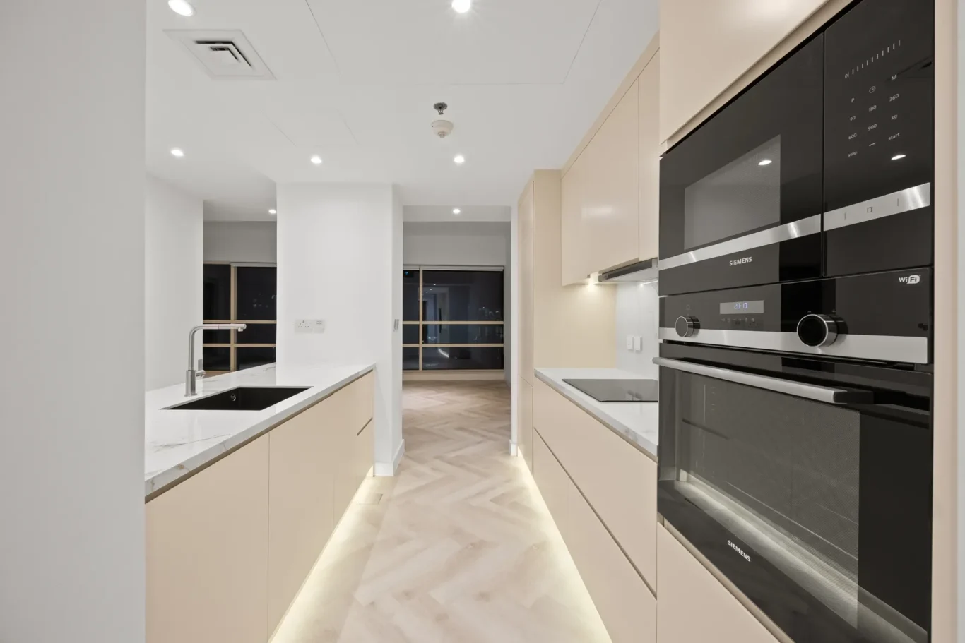 Modern kitchen with beige cabinets, marble countertops, and a built-in Siemens oven unit on the right side