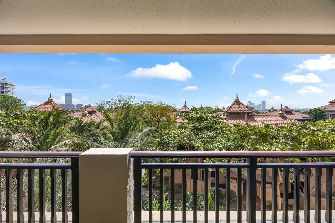 Balcony view of a tropical resort with palm trees and terracotta roof tiles under a bright blue sky.