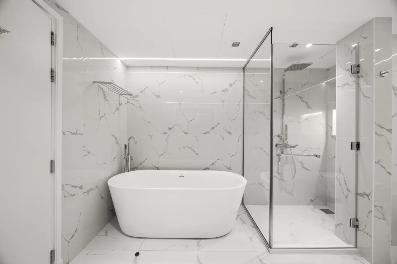 Luxurious bathroom with a white freestanding tub and glass-enclosed shower against marble walls.