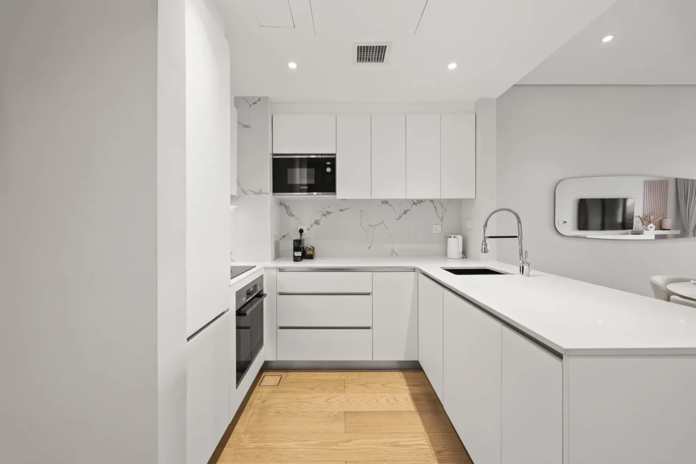 Bright white modern kitchen with island, built-in oven and microwave, marble backsplash, and a stainless sink with gooseneck faucet.