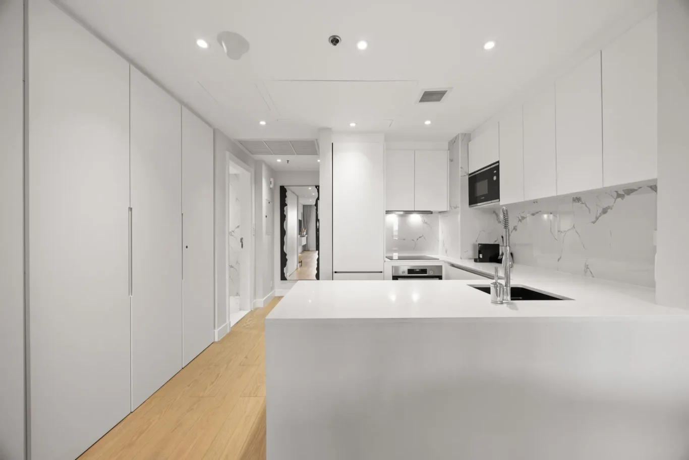 White minimalist kitchen with marble backsplash, island, and built-in oven.