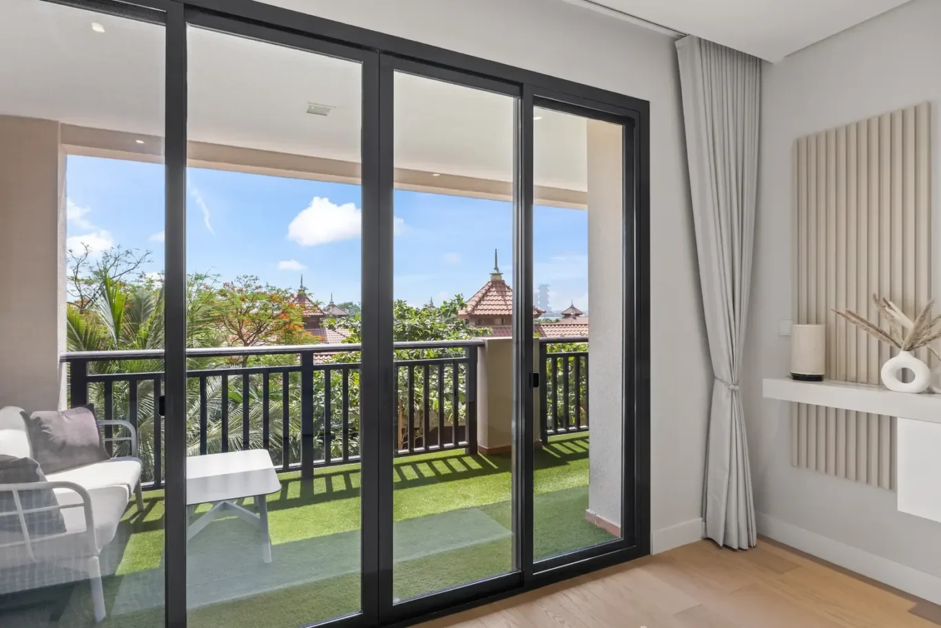 Living room with large glass sliding doors opening to a balcony, with outdoor seating and a green artificial lawn.