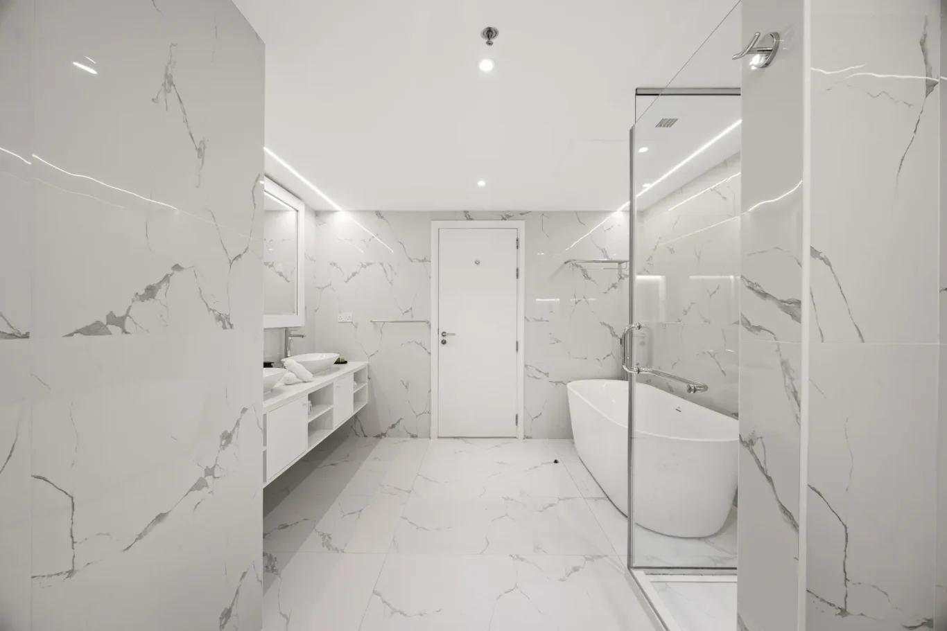 Bright white marble bathroom featuring a freestanding tub, glass shower, wall mirror, and a white vanity.