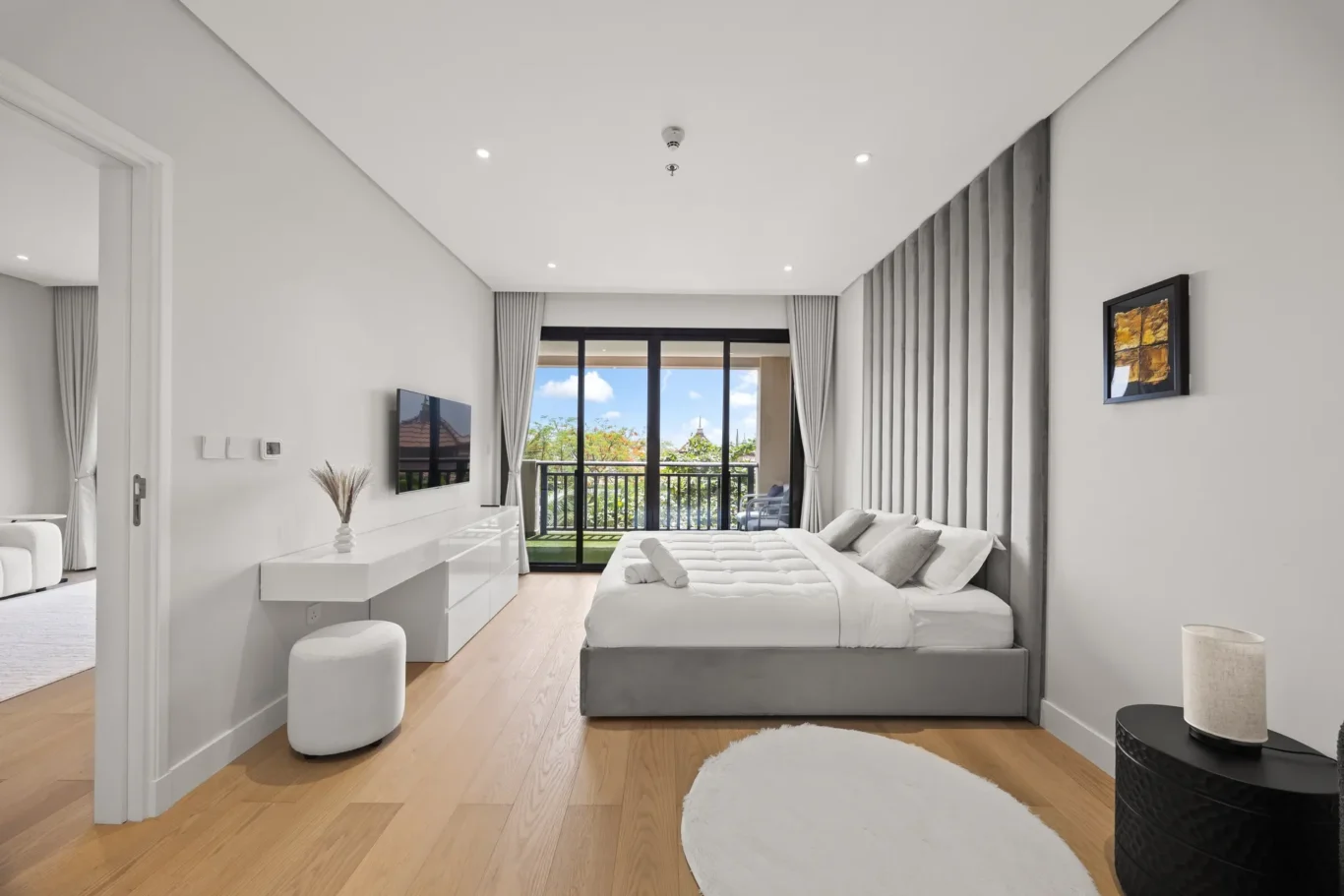 Modern hotel bedroom with two white beds, a grey paneled headboard wall, wall TV, and glass balcony doors.”](")