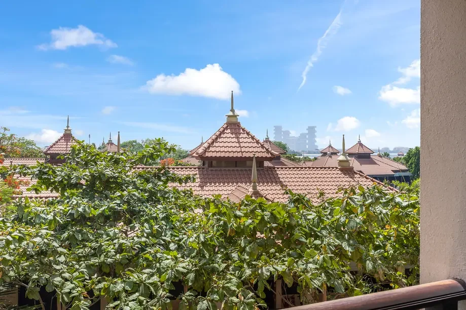 View of brown terracotta temple-style rooftops with pointed spires, greenery in the foreground, and a blue sky above a distant cityscape.