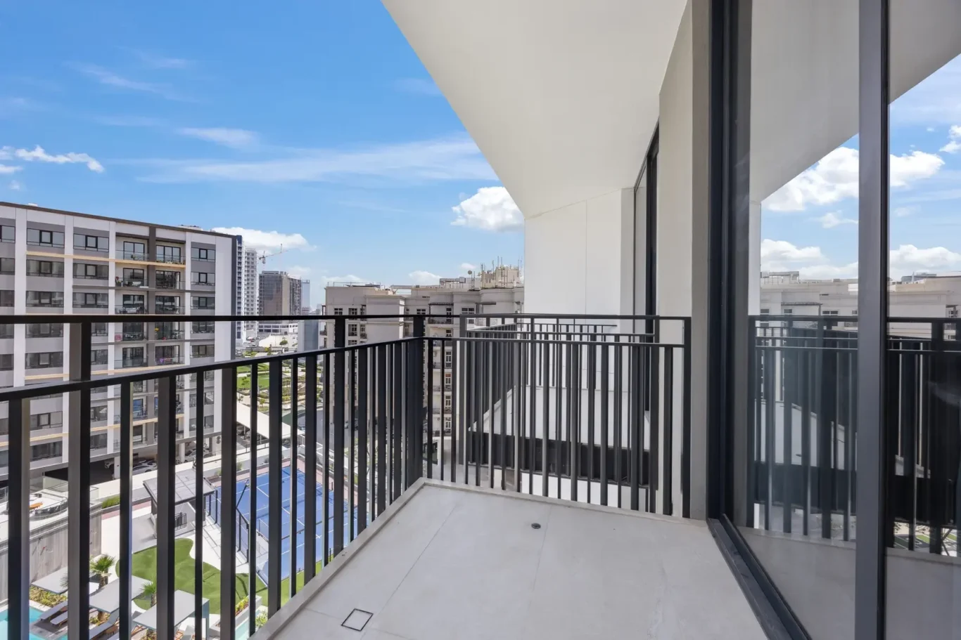 View from a high-rise balcony with black metal railing over a modern apartment complex and a clear blue sky