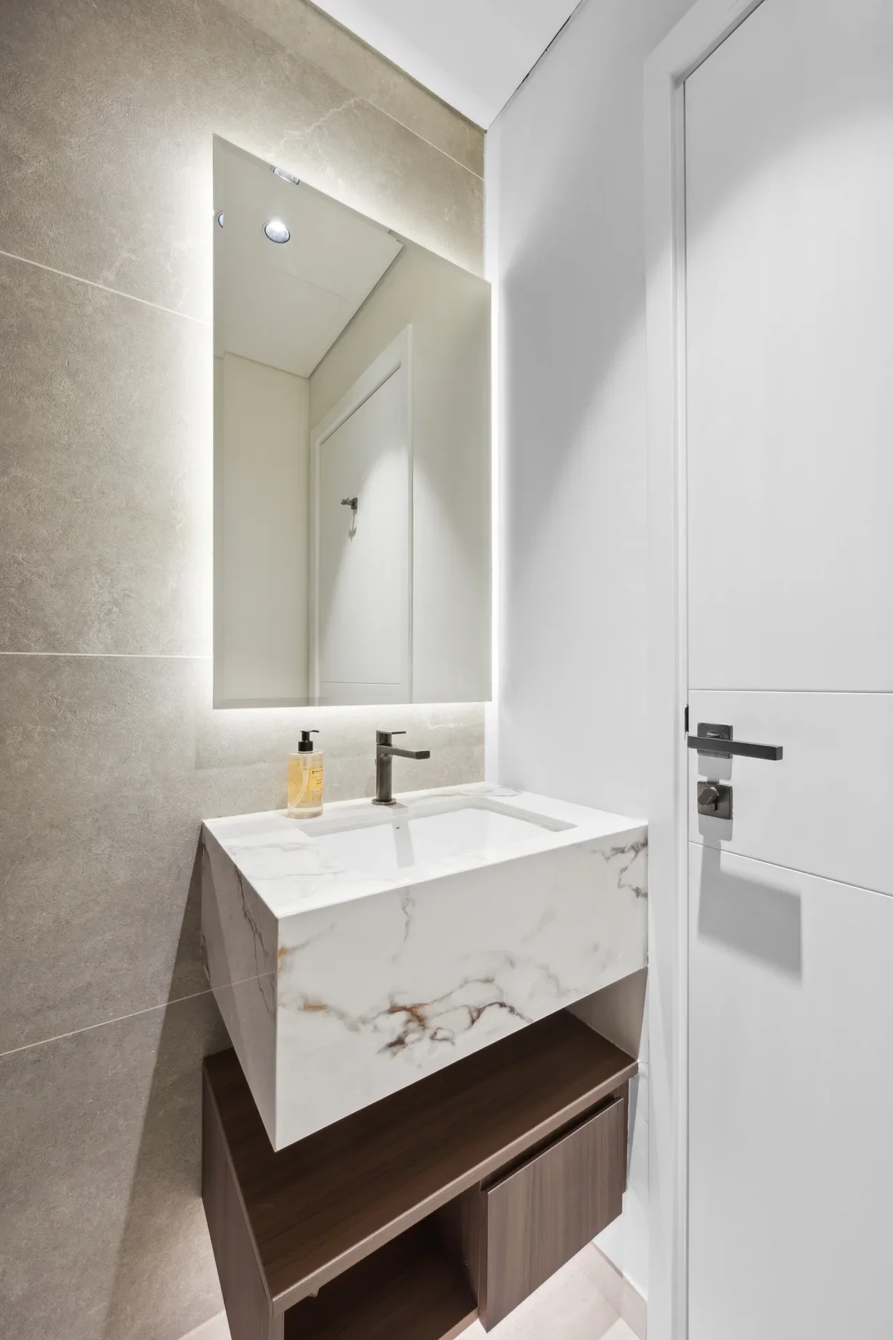 Backlit rectangular mirror above a white marble countertop sink with a dark wooden floating vanity in a modern bathroom.
