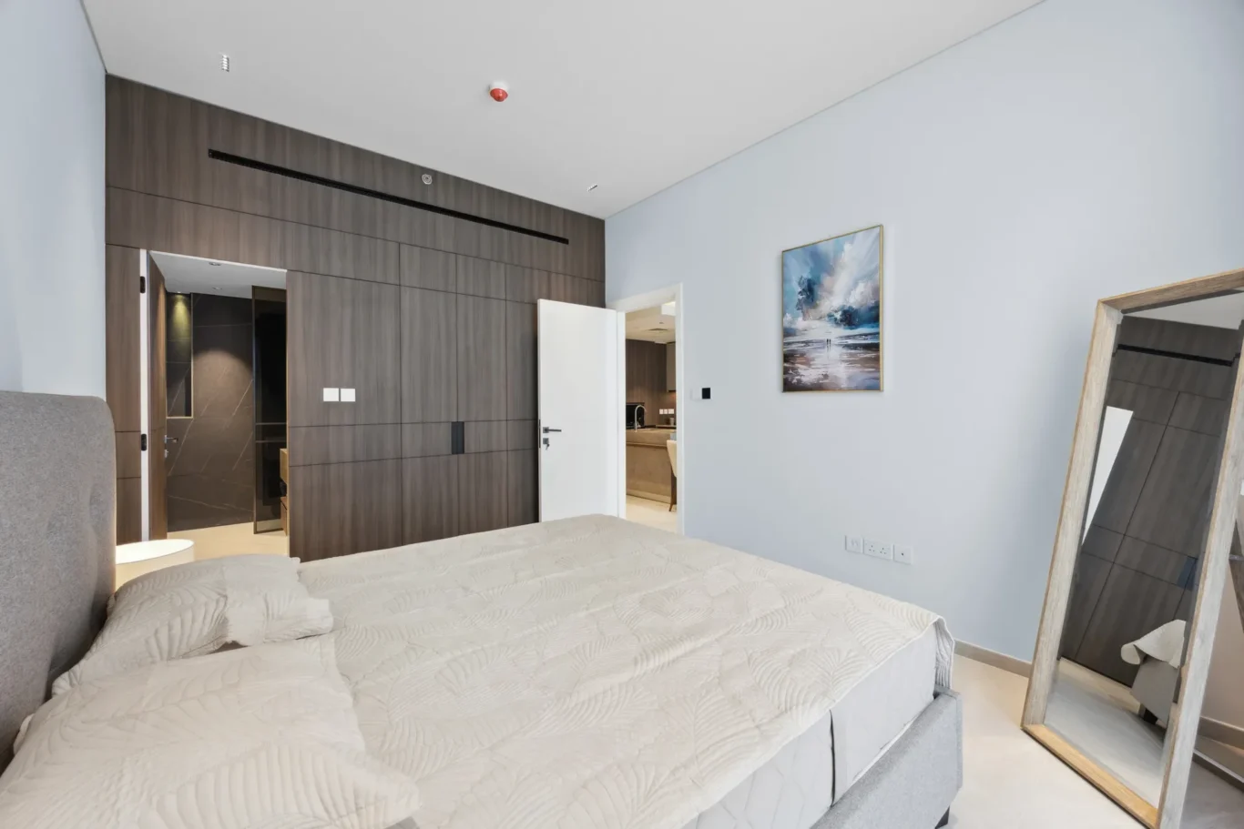 Modern hotel-style bedroom with two beds, white quilted covers, and a gray upholstered headboard; dark wood built-in wardrobes along the far wall.