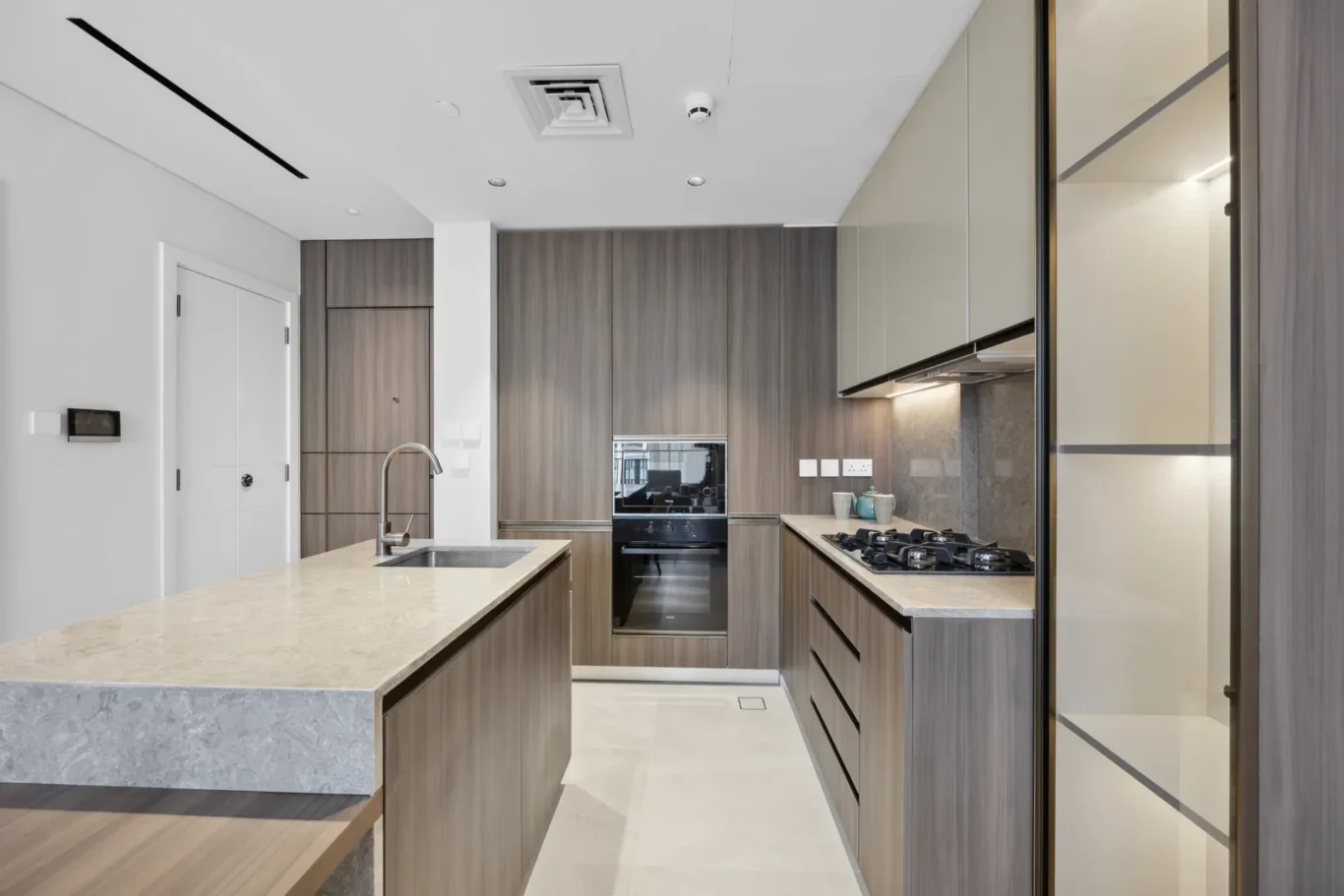 Modern kitchen with wooden cabinets, built-in oven, gas cooktop, and an island sink.