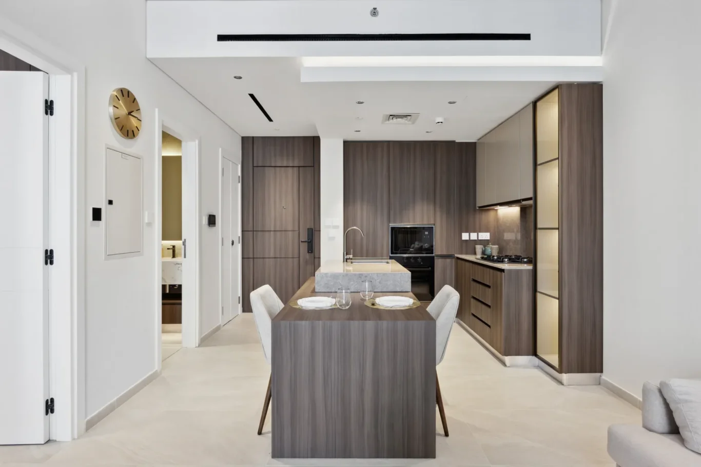 Open-plan kitchen with a central island, dark wood cabinets, and built-in appliances along the wall; a dining table sits in the foreground.