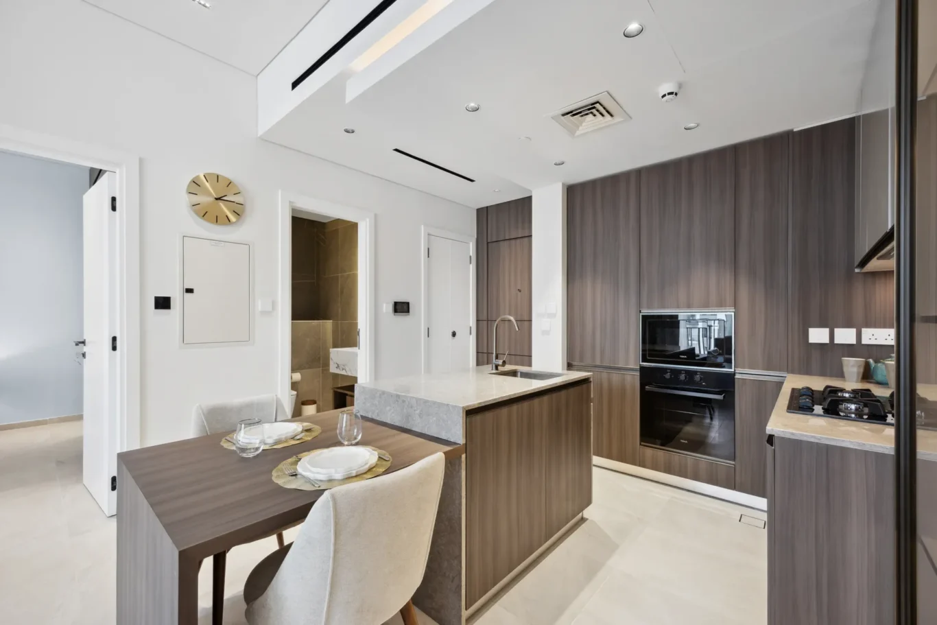 Modern white-and-wood kitchen with island, built-in oven, and gray marble countertops; dining area in foreground.