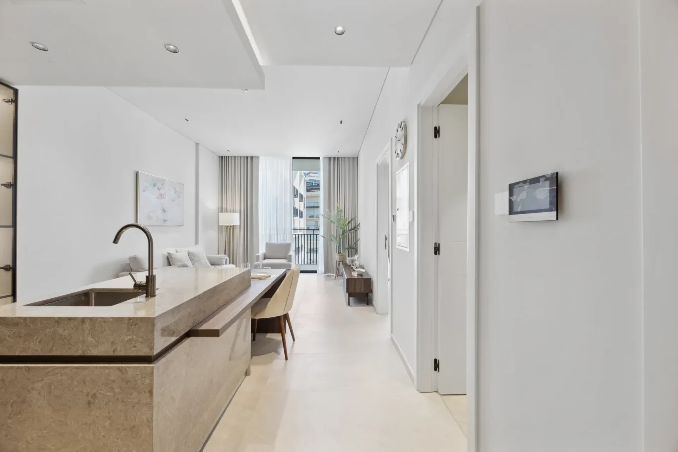 Open-concept living area with a marble kitchen island, sink, and beige stools, leading to a bright seating area by the balcony window.