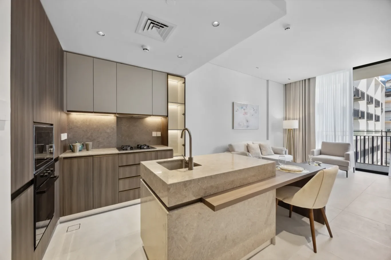 Open-plan kitchen and living area in a modern apartment with a marble island, gray cabinets, and a balcony view.