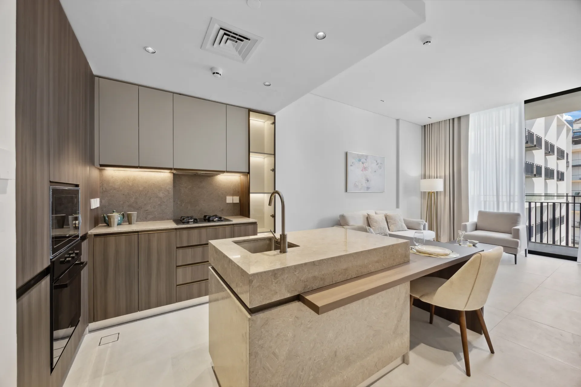 Open-plan kitchen and living area in a modern apartment with a marble island, gray cabinets, and a balcony view.