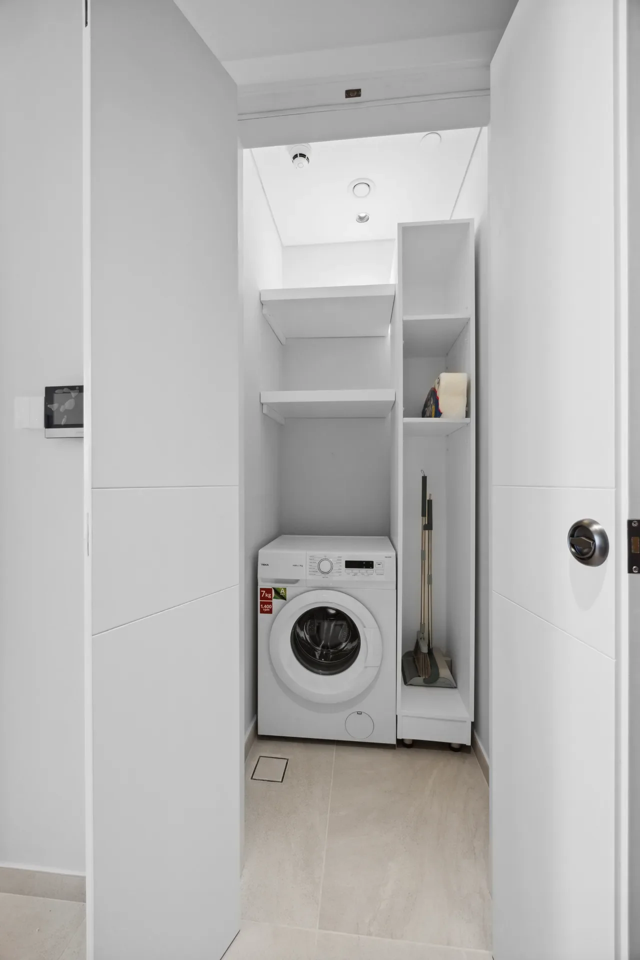 Laundry nook with a front-loading washing machine beneath white shelves and cabinetry.