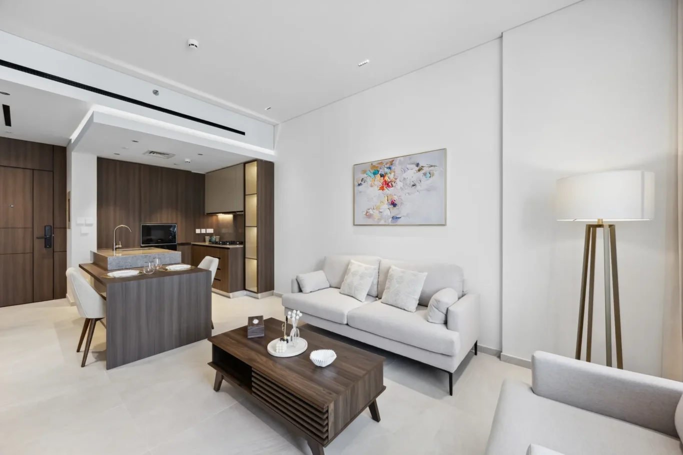 Open-plan living area with a grey sofa, wooden coffee table, and a compact kitchen in the background.