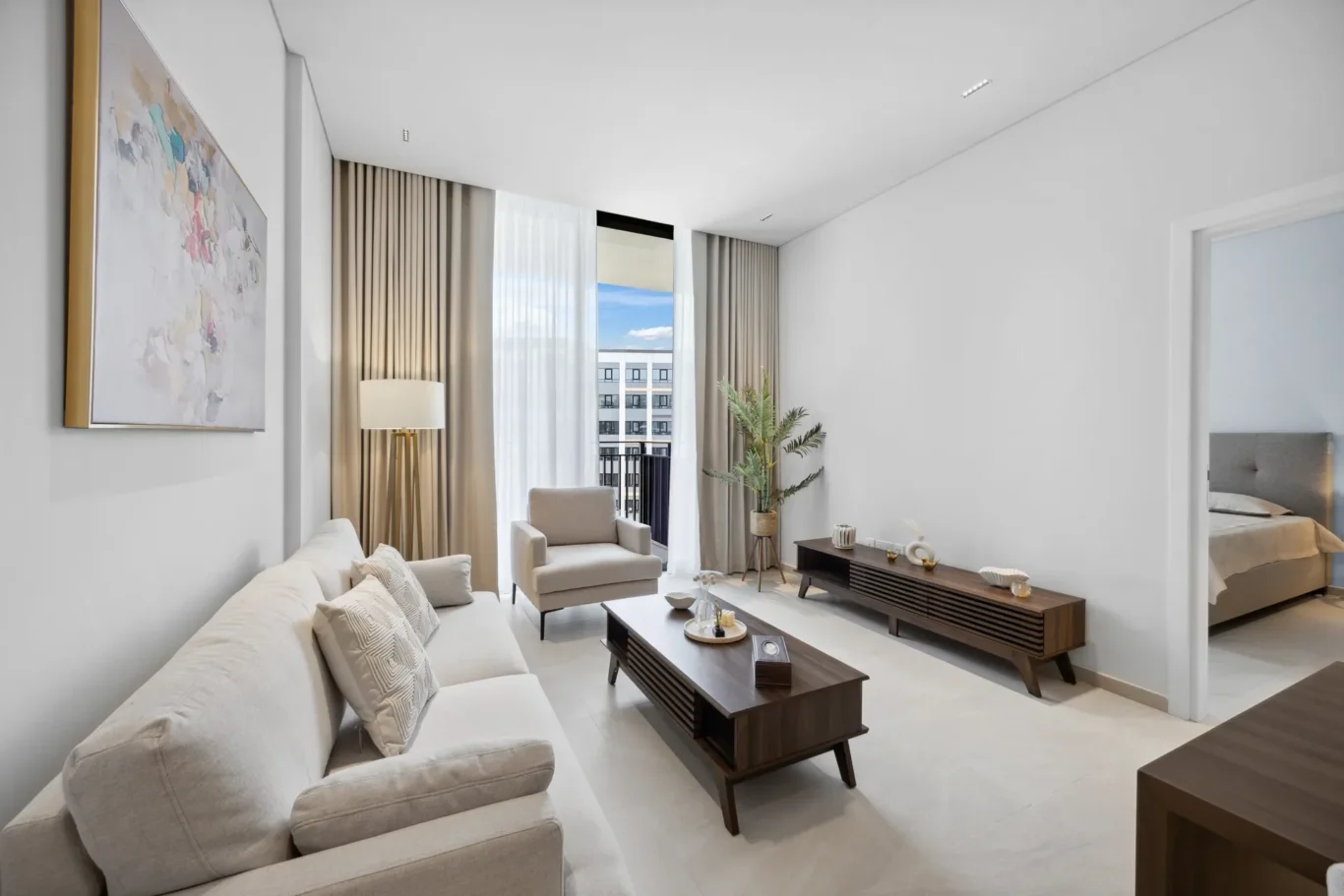 Living room with a cream sofa and armchair, two dark wood coffee tables, a tall floor lamp, and a large window with sheer and beige curtains.