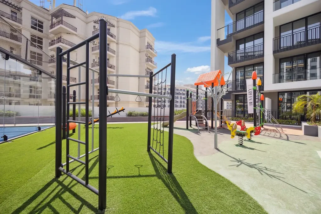 Playground with a metal climbing frame, slides, and a spring rider in a courtyard of modern apartment buildings.