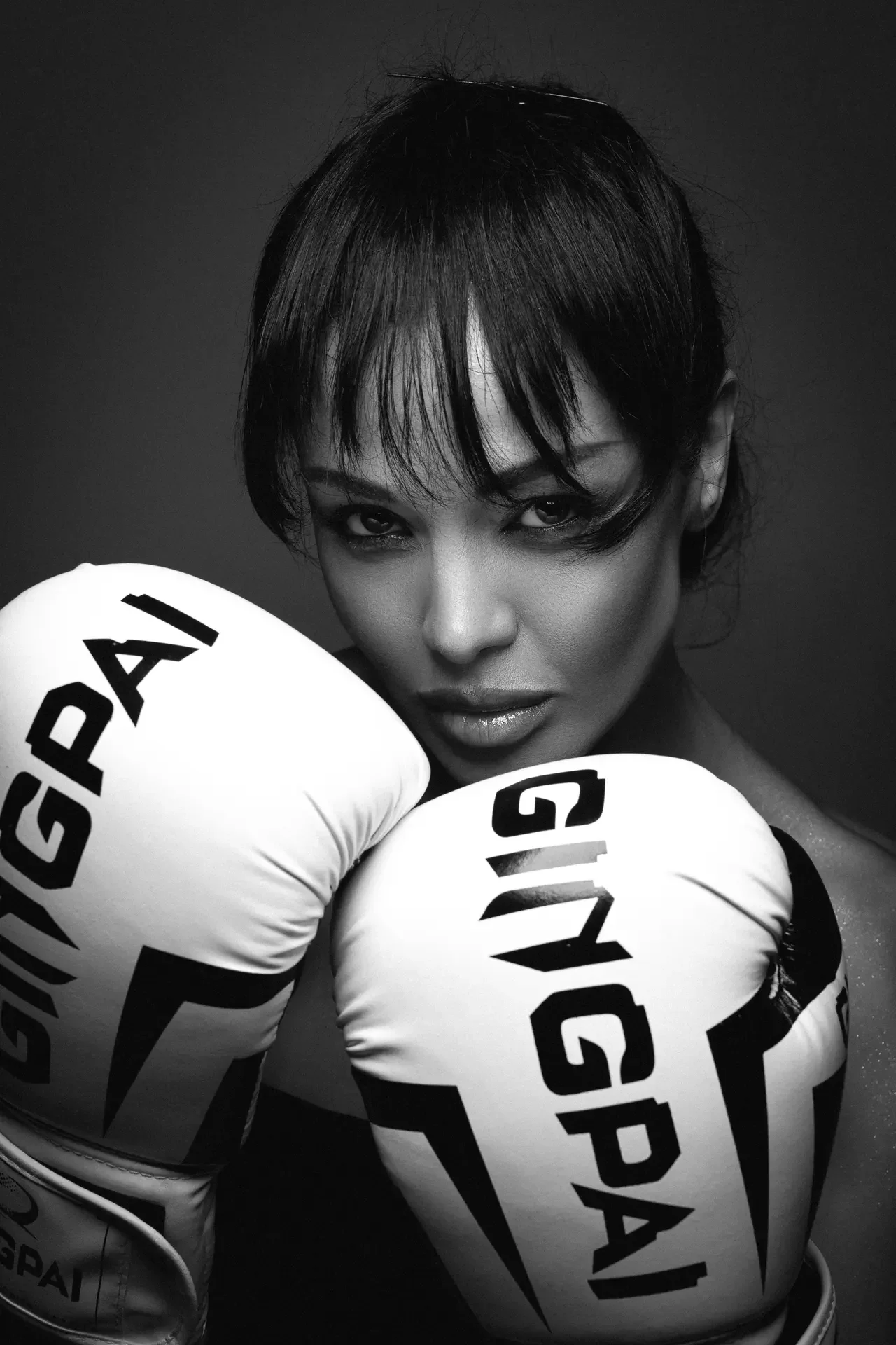 Black-and-white portrait of a woman wearing boxing gloves, facing the camera with a determined expression.