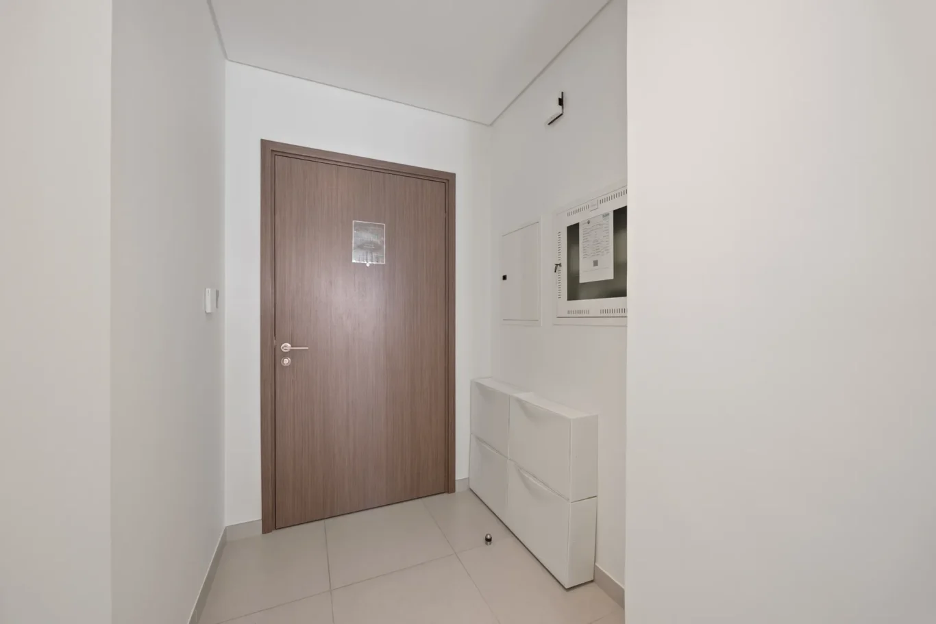 Narrow hallway with a brown wooden door on the left and a white laundry area on the right, including drawers and a front-loading appliance.