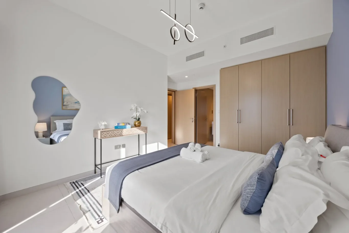 Twin beds in a bright hotel room with white linens, blue accents, and a wall of wooden wardrobes to the right.