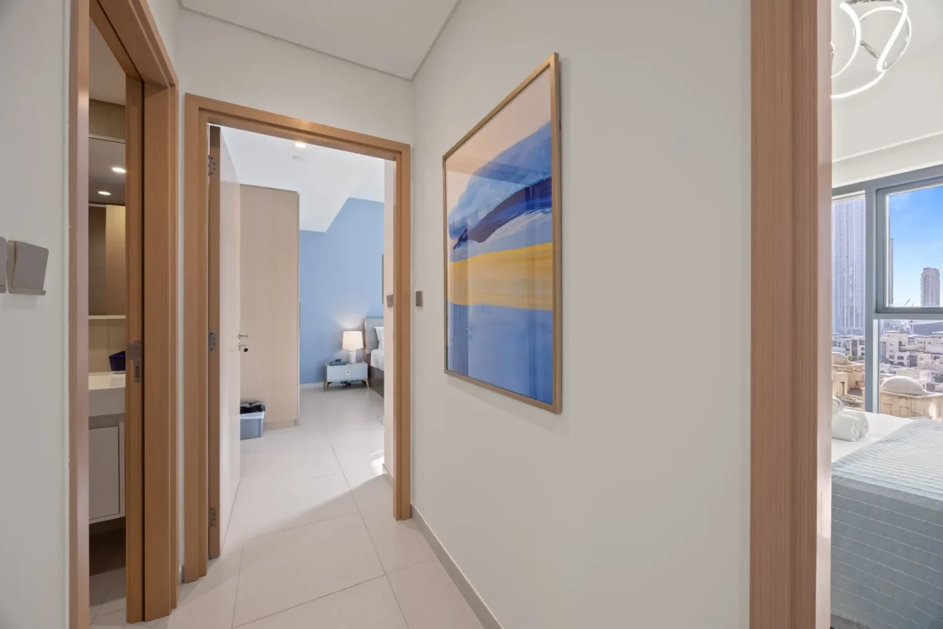 Hallway of a modern apartment with an open door to a bedroom featuring a blue accent wall, a nightstand and lamp visible in the room.