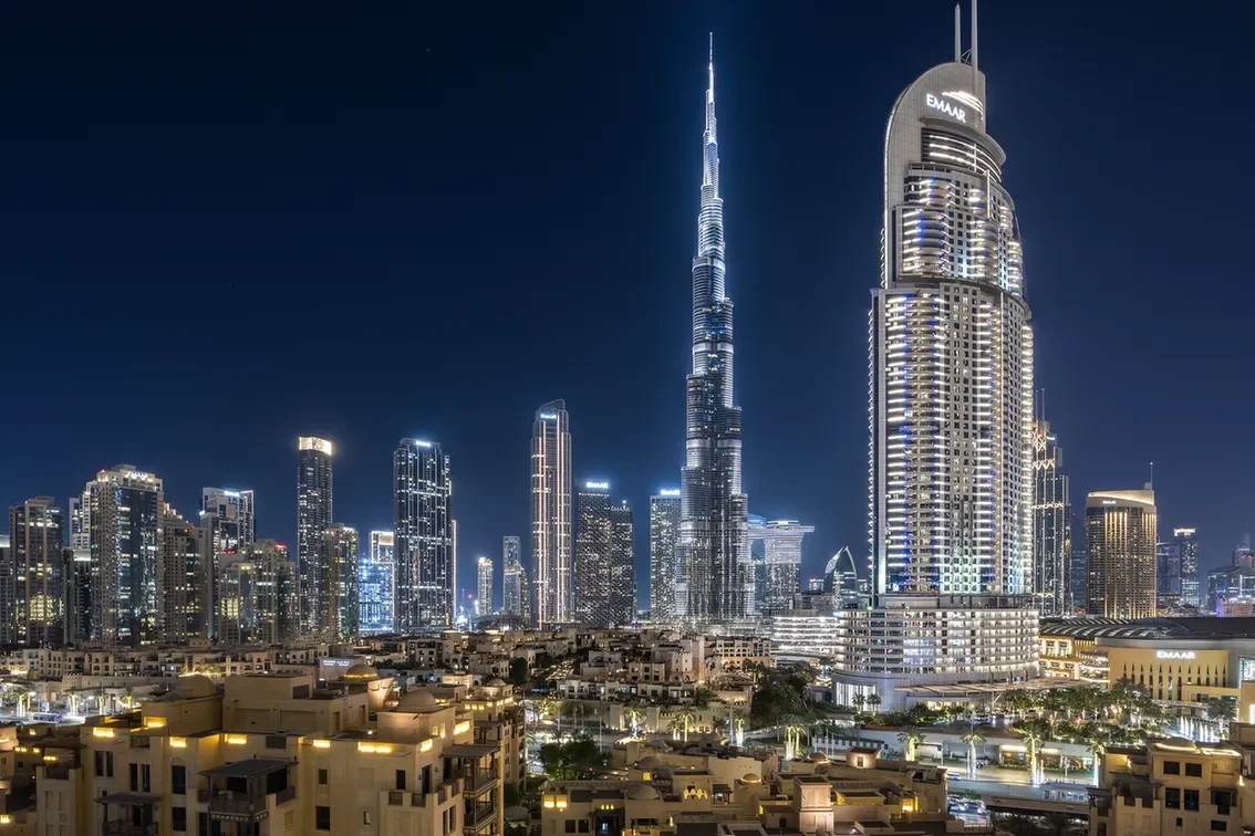 Nighttime Dubai skyline with the Burj Khalifa towering over illuminated skyscrapers.