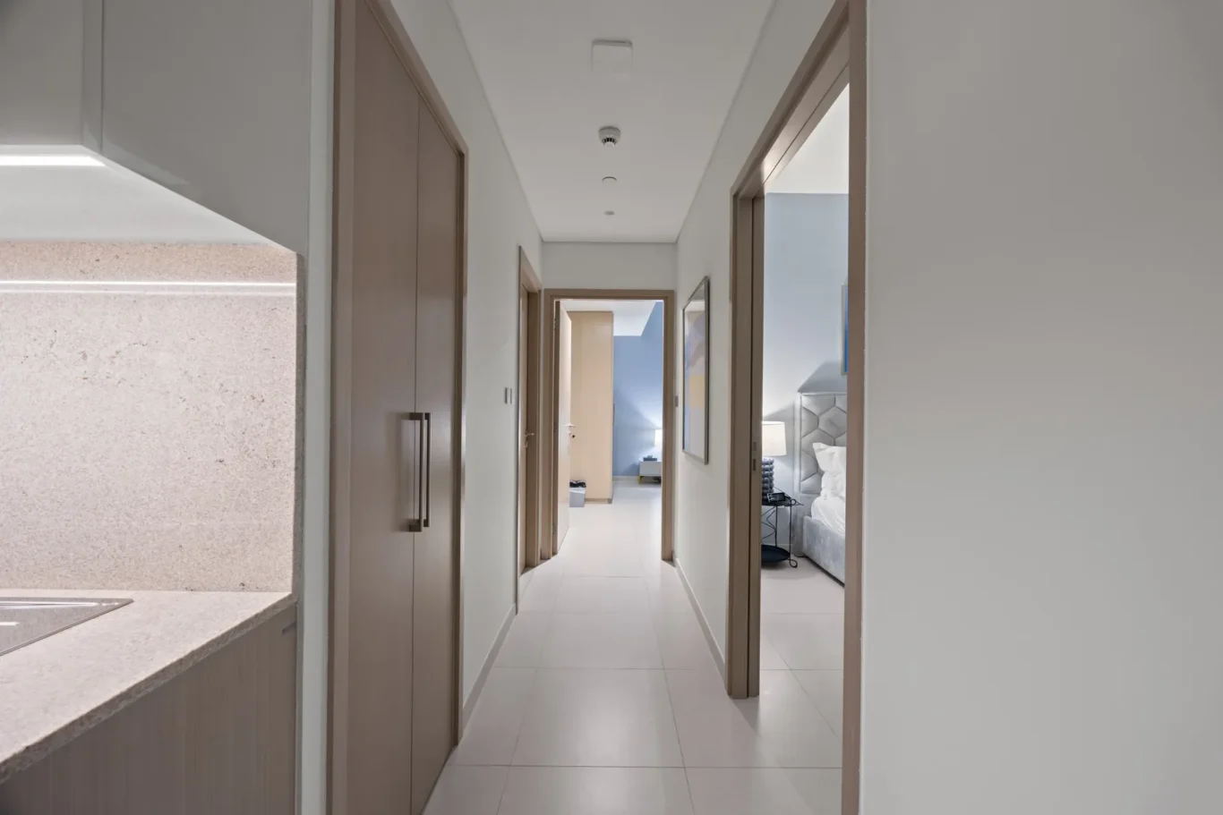 Bright, minimalist hallway in a modern apartment with wooden doors and a view into a bedroom at the end
