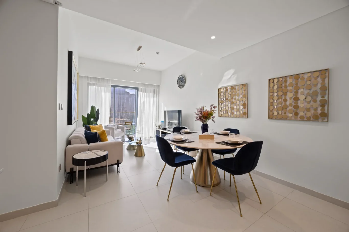 Open-concept living and dining area with a round marble table, blue chairs, beige sofas, and circular wall art.