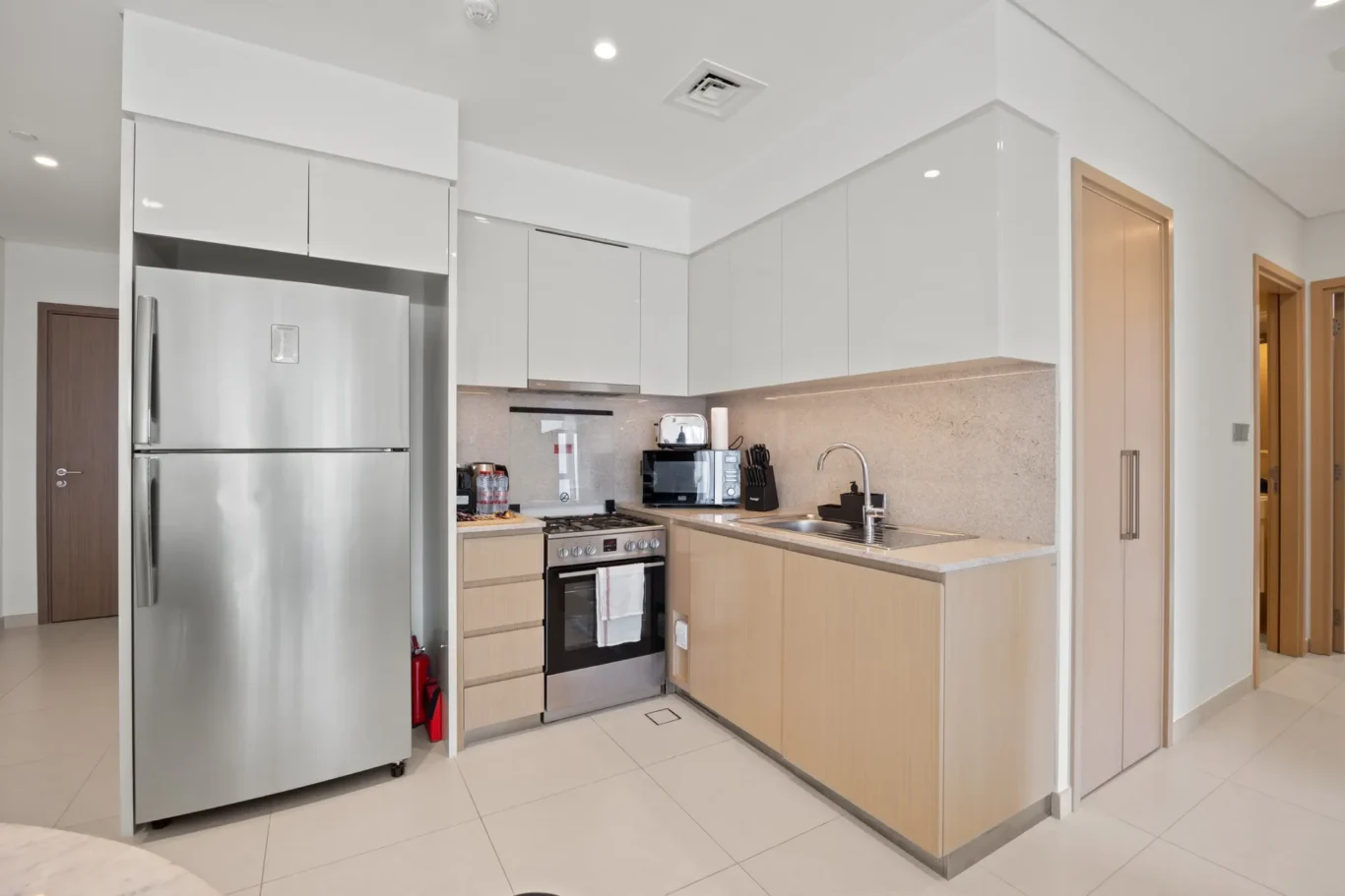 Modern white kitchen with stainless steel refrigerator, gas range, and beige stone backsplash.
