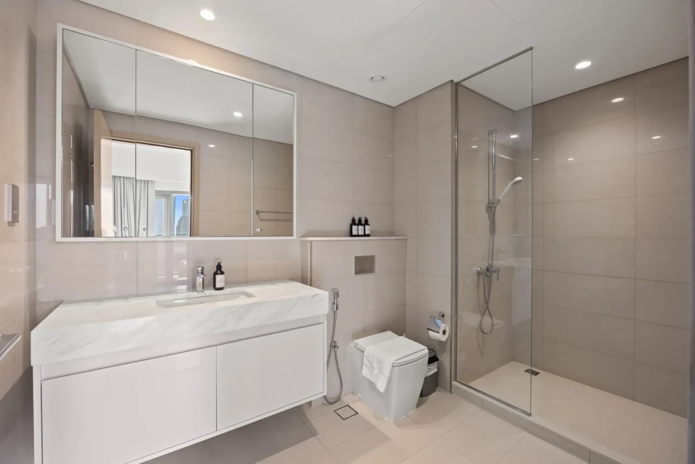 Modern bathroom with a marble countertop vanity, large mirrored cabinet, wall-hung toilet, and glass-enclosed shower.