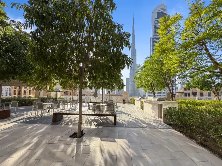 Open-air terrace with trees and seating, overlooking a city skyline including skyscrapers like Burj Khalifa on a sunny day