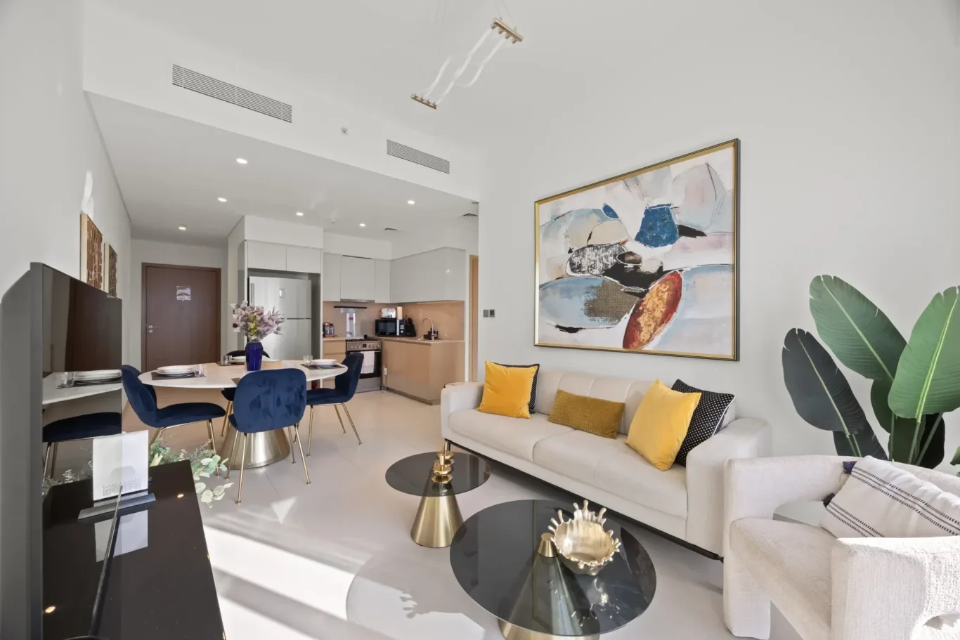 Open-plan living and dining area with white walls, blue chairs, and a large abstract painting on the wall