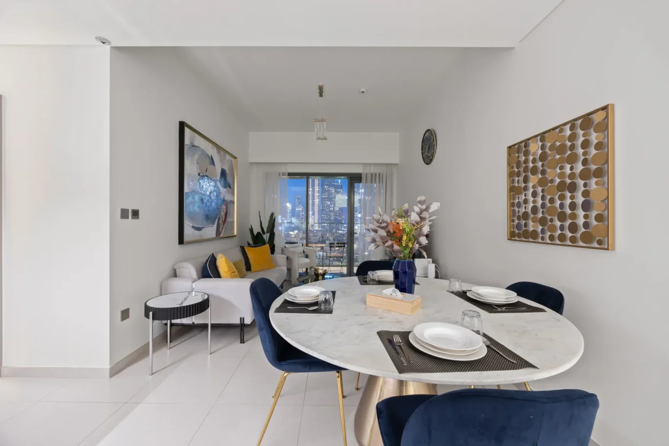Open-plan dining area with a marble table set for six, blue velvet chairs, and a city skyline visible through sliding doors in the back.
