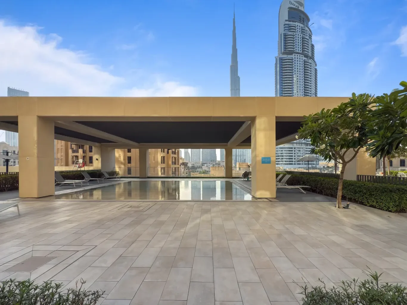 Rooftop pool under a beige pergola with lounge chairs, overlooking Dubai's skyline including the Burj Khalifa.