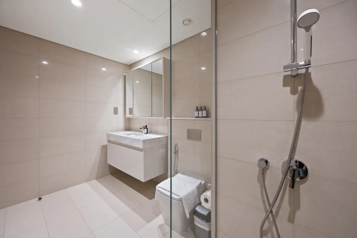 Modern bathroom with wall-mounted white vanity, mirrored cabinet, and beige tiled walls and floor